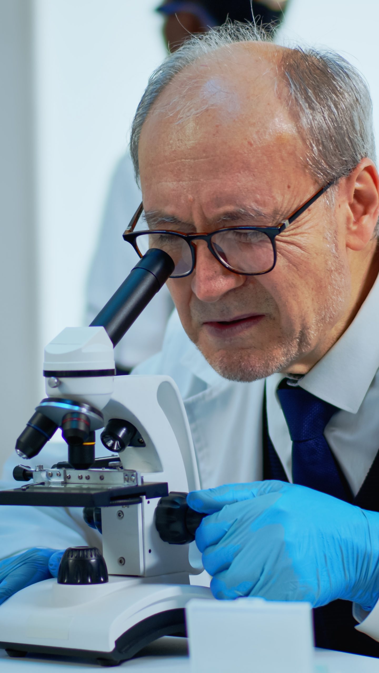 Laboratory scientist conducting experiment looking at microscope in busy lab